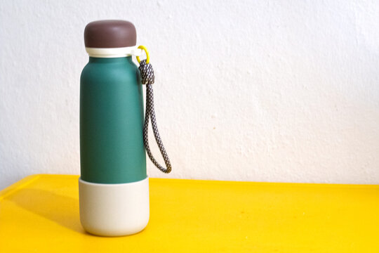 A steel thermos on a yellow table. Vacuum container or bottle for hot and cold water. Camping thermos. Student water bottle. Left-aligned for the text area. 