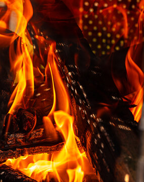 Close-up view of vibrant flames consuming wooden logs in a fireplace, with glowing embers and a blurred background of a decorative screen