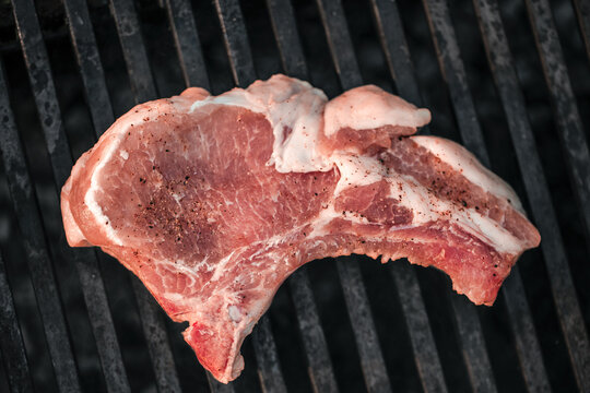 Raw pork chop seasoned with black pepper resting on a grill rack, showcasing grill marks and a textured surface in a cooking environment