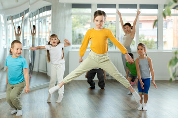 Fototapeta premium Girl engaged jumping into air in fitness studio with friends, group of youthful friends bob up and down during dance class. Children in good mood actively move and dance at choreography.