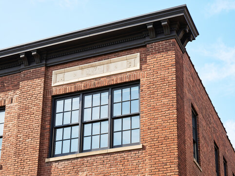 Corner view of a red brick building with black framed windows, dark cornice, and a light stone lintel against a clear blue sky