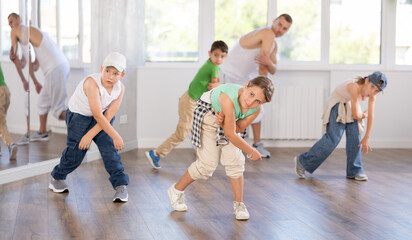 Fototapeta premium Expressive happy young girl learning modern street dancing during group class in choreographic studio