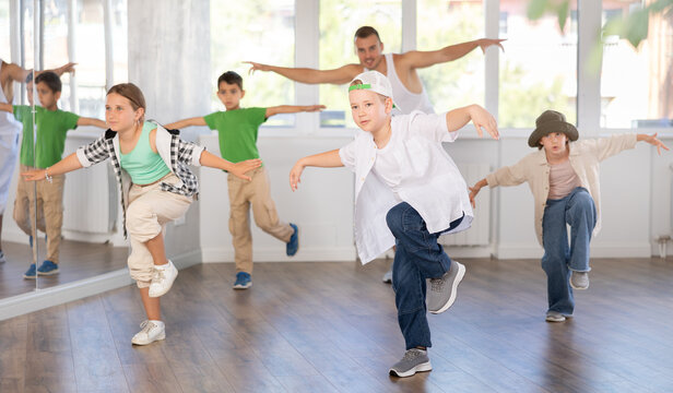 Emotional tween boy dancer rehearsing modern krump dance moves during group workout in kids studio under guidance of male instructor