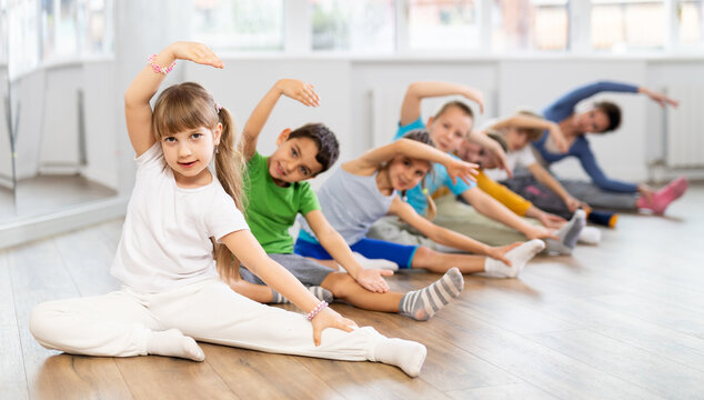 Little school age children learn to do dance moves on the floor in a choreography studio
