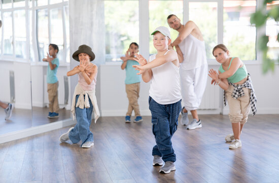 Emotional tween boy dancer rehearsing modern krump dance moves during group workout in kids studio under guidance of male instructor