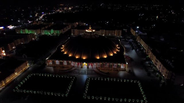 Aerial drone view of the beautifully illuminated Prem Mandir in Vrindavan, India, during Janmashtami celebrations at night. The magnificent temple glows with colorful lights that continuously change.