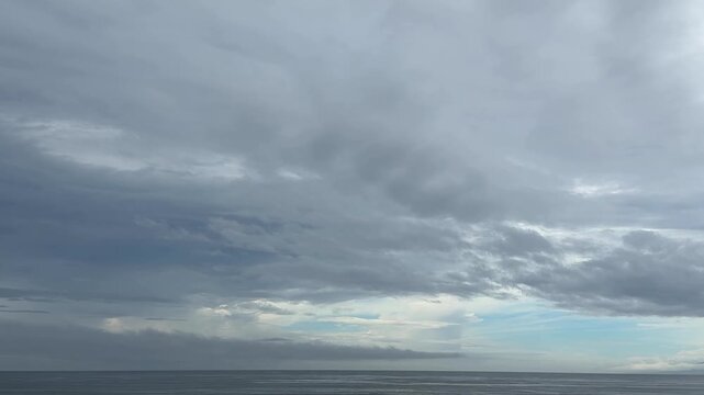 流れる雲の広がる灰色の空と穏やかな水平線