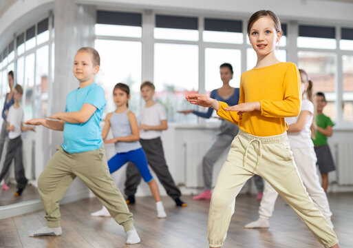Dynamic little girl training hip hop dance poses with instructor and other attendees of dancing courses