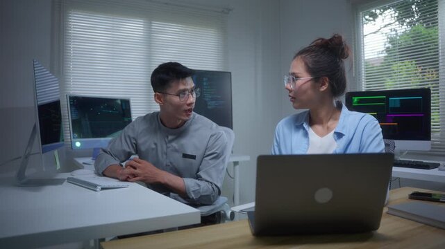 Asian IT developers coding and collaborating in a modern office while working late on a software project