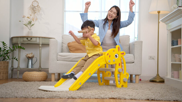 Happy little boy sliding down with laughter while his mother watches nearby