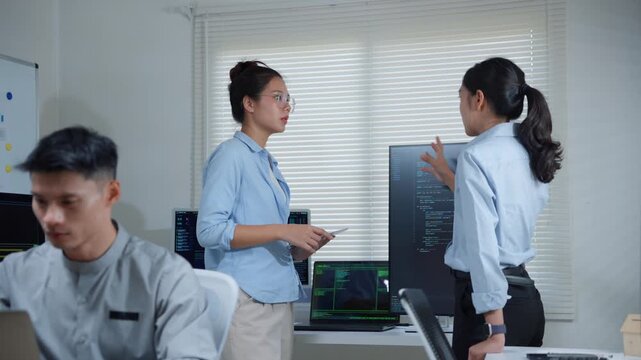 Asian women developers collaborating on code, discussing software development project in a modern technology company office