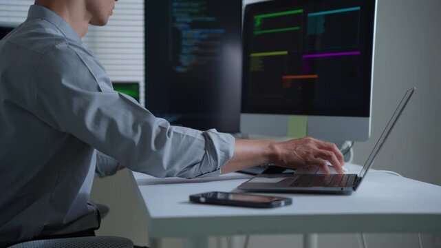 Focused software developer writing code at night on multiple computer monitors in a modern office