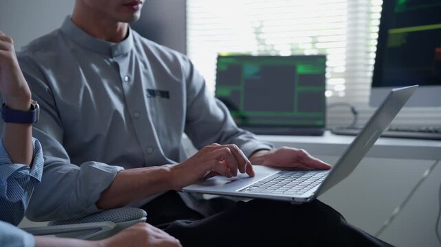Close up of software developers brainstorming ideas and programming on a laptop in a modern tech office with multiple screens