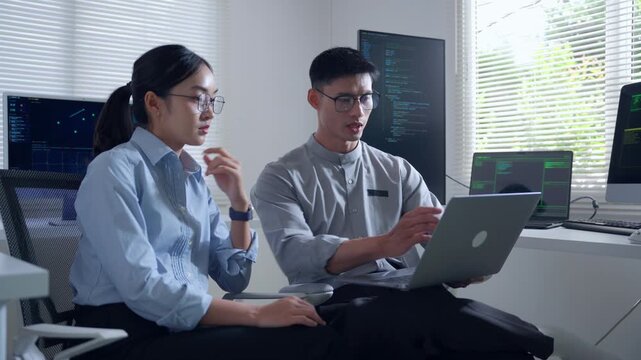 Asian IT developers discussing software code on a laptop in a modern office, teamwork and programming concept