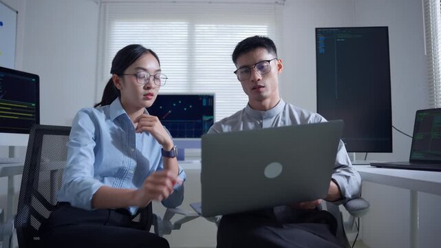 Frustrated programmer crumpling paper after coding error with his colleague in a tech office at night