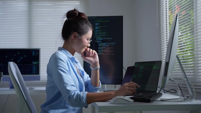Female programmer coding at night using multiple computer screens and thinking about a solution for a new application