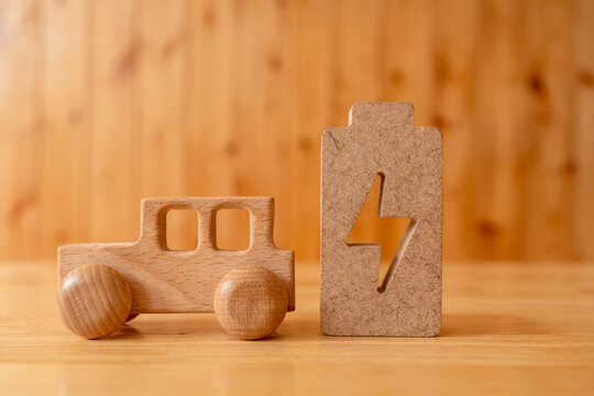 Electric vehicle battery charging concept with wooden car model standing beside wood battery symbol with lightning icon, representing clean renewable energy, eco transportation, and green mobility.