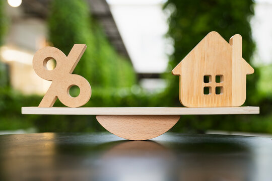 Real estate property mortgage loan interest rate balance concept, wooden percentage sign and house model on seesaw scale, showing home loan refinance dilemma and housing affordability cost.