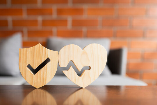 Health insurance and medical care protection concept with wooden shield and heart pulse rate shape standing together on table, representing wellness guarantee, life safety, and hospital coverage.