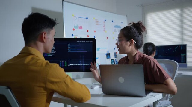 Asian programmers discussing code while working late in a startup office on a new software development project