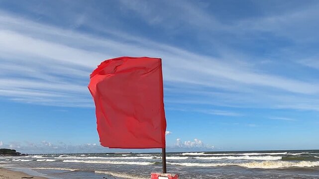 Red beach warning flag fluttering in wind beside rough sea