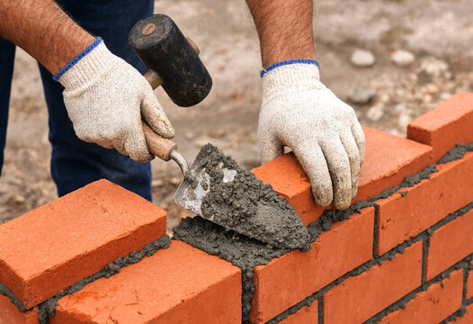 Construction Worker Applying Mortar Between Red Bricks Using Trowel