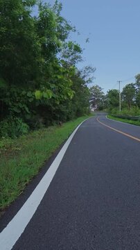A winding mountain road through lush green forest with a prominent left turn warning sign, clear asphalt and a scenic outdoor setting.