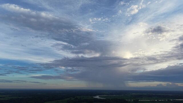 Aerial view of rain shower over rural landscape and winding river at sunset drone storm