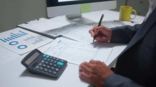 Businessman working on financial report using a calculator and writing on documents at his desk in the office