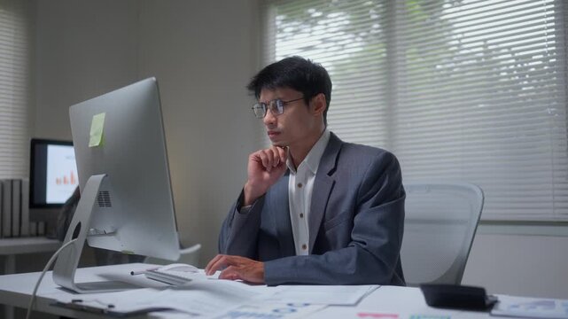 Happy asian businessman analyzing data and celebrating successful financial report results at his modern office desk