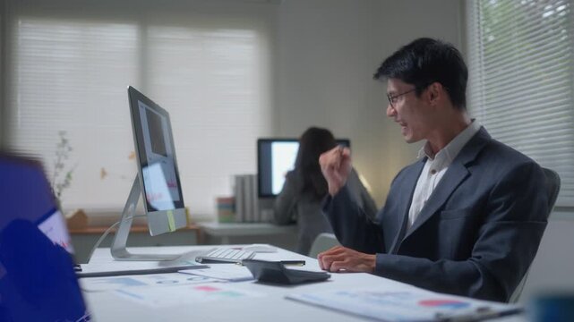 Asian businessman celebrating success during a video conference while working late in the office