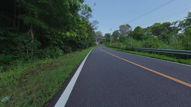 POV cycling along a winding mountain road surrounded by lush tropical forest, roadside vegetation, guardrails and clear blue sky, creating an immersive scenic journey.