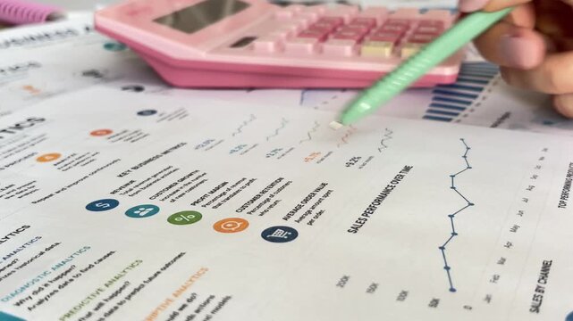 Financial analyst calculating company sales performance and business analytics using a calculator and examining corporate charts and graphs on a financial report