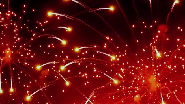 The footage shows bright fireworks in black night sky. The view includes bright red gold green or white sparks forming circular and branching light patterns within black night sky.