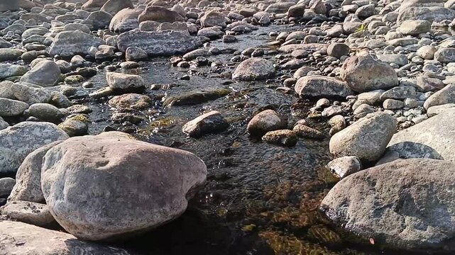 Shallow river stream trickling through rocky terrain during dry season. Ideal for climate change, drought awareness, environmental ecology documentaries, and natural background scenes