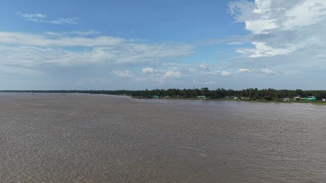 Aerial view of wide tropical river and lush green riverbank under blue sky with clouds drone landscape
