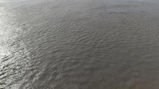 Flowing river water surface texture with gentle ripples and sunlight reflections