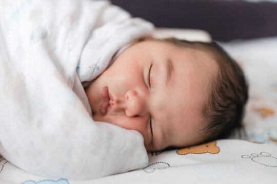 Sweet newborn baby lying comfortable asleep on side wrapped snugly in soft muslin wrap.