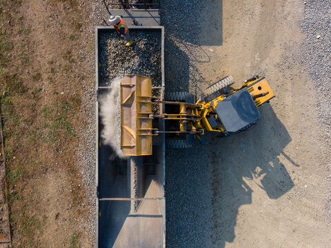 Aerial Construction work of a Yellow Wheel Loader Loading Ballast Rock into a Railway Transport Wagon with Workers Visible on Top in Karangsari, Indonesia. Maintenance Operation Shows Heavy Machinery 