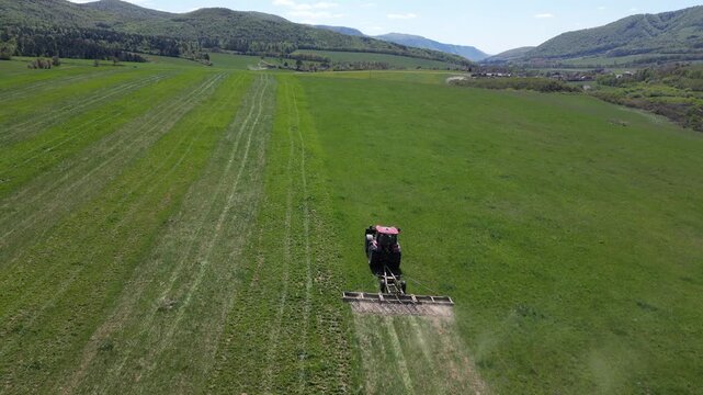 Aerial view of a tractor with a harrow cultivating a vast green field. The agricultural machine prepares the soil for spring planting