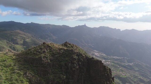A captivating aerial drone push in shot revealing the rugged volcanic landscape on Gran Canaria, Spain. The vista features winding roads, mountain villages, and Roque Nublo.