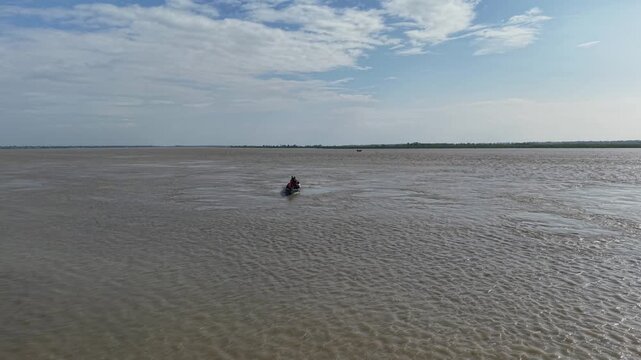 Small motorized boat navigating wide tropical river, aerial view of local water transportation in remote region