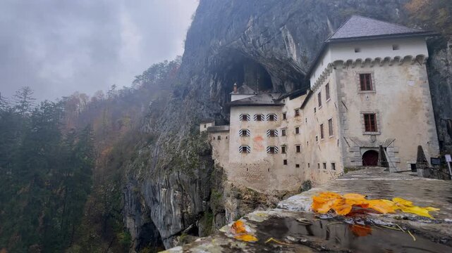 Stunning view of the historic Predjama Castle, a medieval fortress built into the mouth of a cave on a cliff during a moody autumn day