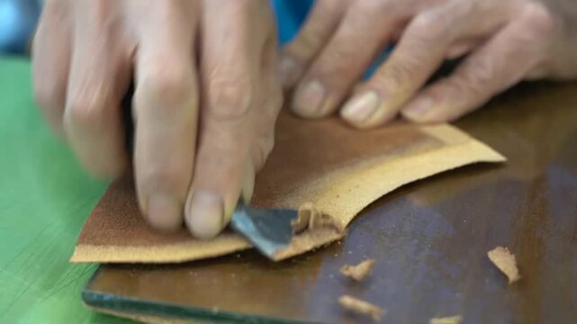 Cobbler hands roughing the edge of a tan leather panel with sandpaper on a green mat to prepare the surface for gluing