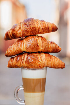 Three fresh croissants stacked on top of a glass of latte