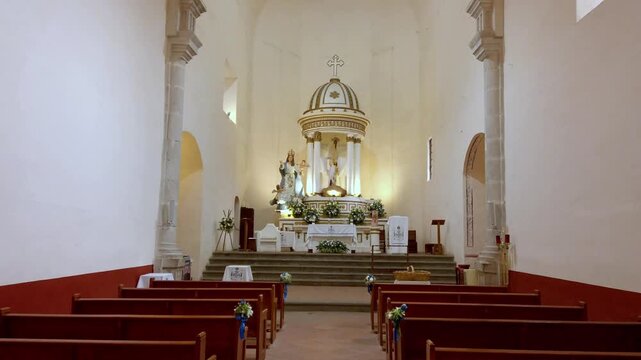 Interior view of a Catholic church showing an ornate altar beneath a domed canopy. Wooden pews line the central nave while stone columns and religious artwork surround the sanctuary
