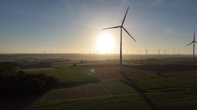 A wide view shows wind turbines above fields near Paderborn, with morning sunlight illuminating patches of low mist across the farmland.