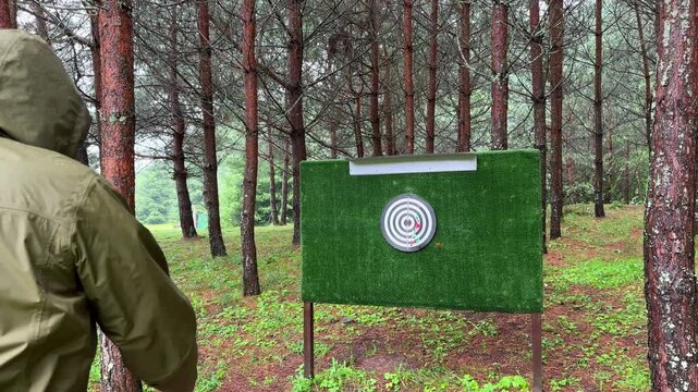 Man aiming a dart toward a target in the woods. Recreational moment captured outdoors during a leisurely forest game. Nature scene showing focus and steady hand control..