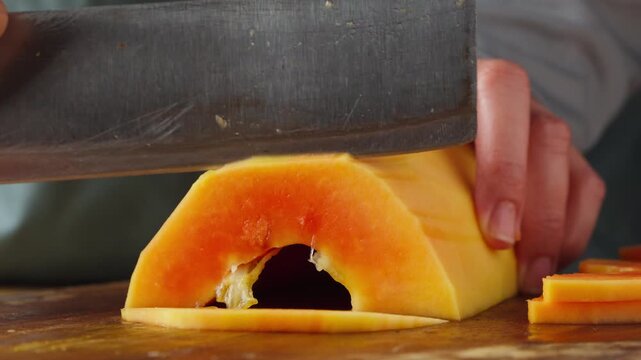 Person thinly slicing fresh unripe papaya on a wooden cutting board