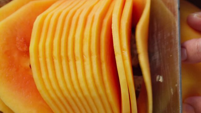 Person thinly slicing fresh unripe papaya on a wooden cutting board